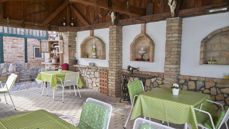 Terrasse, Gästezimmer Victoria, © Marianne Graf Überdachte Terrasse mit grünen Tischdecken, weißen Stühlen und rustikaler Dekoration.