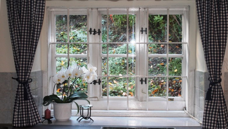 Ferienwohnung Fam. Holzer, © Familie Holzer Fenster mit karierten Vorhängen und einer Orchidee auf der Fensterbank.