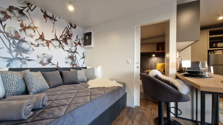 Couch Johannesbachklamm Chalet, © Johannesbachklamm Chalet Innenansicht eines modernen Chalets mit grauem Sofa, dekorativer Blumenwand, Barhocker und Esstisch.