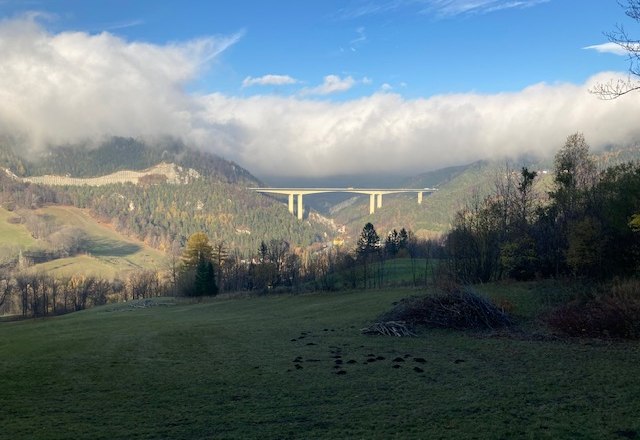Ausblick, © Thomas Ruzicka Landschaft mit Brücke über ein Tal, umgeben von bewaldeten Hügeln und Wolken.