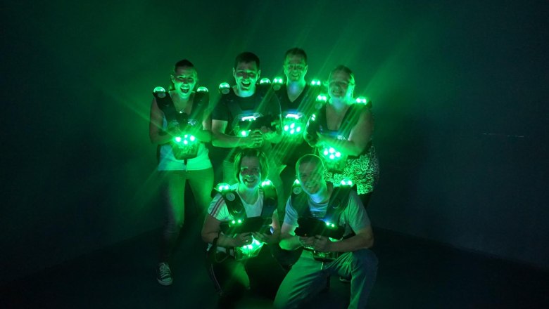 Lasertag Game Team, © Suracon OG Gruppe von sechs Personen in Lasertag-Ausrüstung mit grünen Lichtern in einem dunklen Raum.