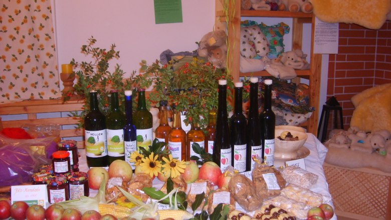 Farm store at the Kölbel organic sheep farm, © Kölbel A table in a farm store with various organic products such as apples, jams, juices and liqueurs, decorated with flowers and plants.