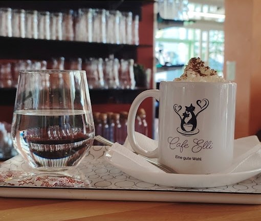 Cafe Elli, © Cafe Elli Ein Tablett mit einem Glas Wasser und einer Tasse mit einem Heißgetränk mit Schlagobers im Cafe Elli.