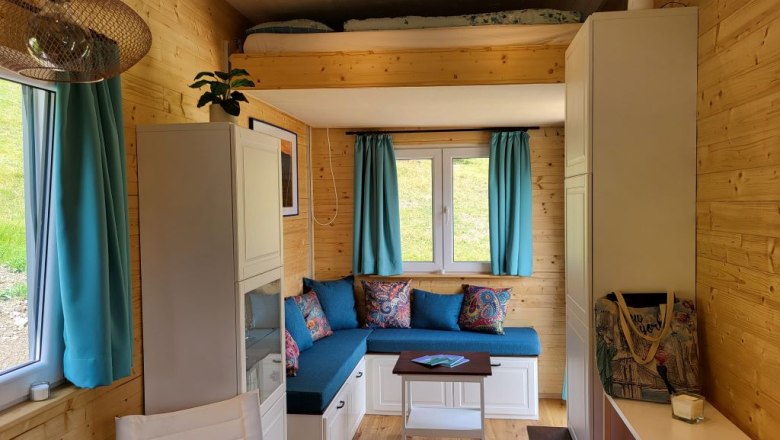 Wohnbereich mit Hubbett, © Villa to go Kleiner Wohnbereich mit Hubbett, blauen Vorhängen und Holzwänden.