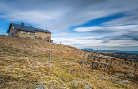 Das Wetterkoglerhaus am Hochwechsel, © Wiener Alpen, Christian Kremsl Das Wetterkoglerhaus auf einem Hügel mit bewölktem Himmel im Hintergrund.