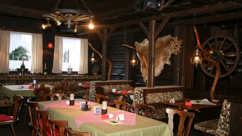 Preiner Stadl, © Scharfegger’s Raxalpen Resort Rustikales Restaurant mit Holzmöbeln, karierten Tischdecken und dekorativen Elementen wie Wagenrädern und Tierfell an den Wänden.