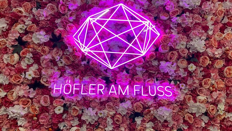 Höfler am Fluss, © Wiener Alpen Pinker Neon-Schriftzug 'Höfler am Fluss' vor einer Wand aus rosa Blumen.