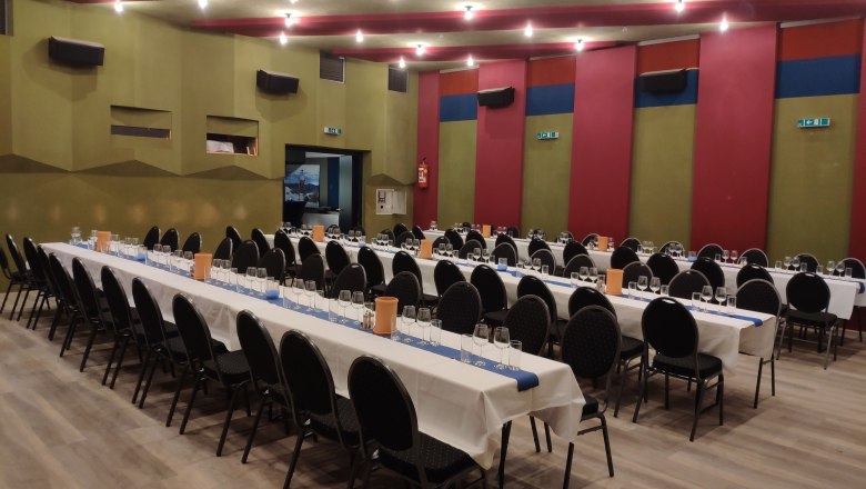 Table in the hall, © Markus Kiener A large hall with long, laid tables and black chairs, ready for an event.