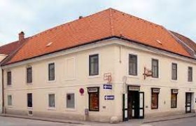 Bäckerei Kustor, © Bäckerei Kustor Eckgebäude mit rotem Ziegeldach und mehreren Schildern, darunter eines mit der Aufschrift 'Bäckerei'.