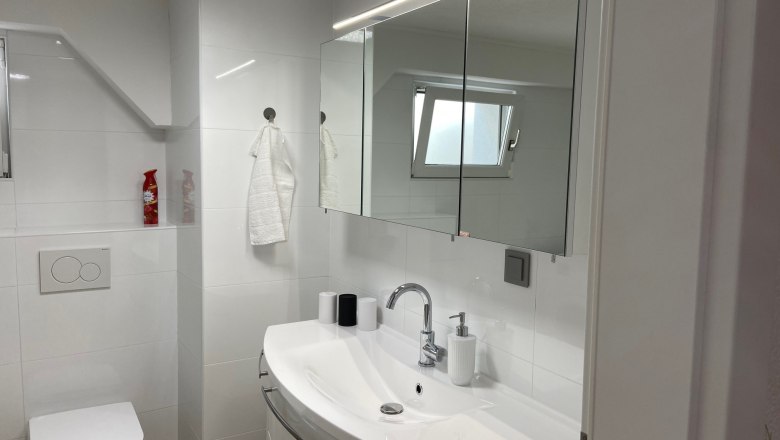 Badezimmer mit Dusche und Waschmaschine, © Wiener Alpen Modernes Badezimmer mit Waschbecken, Spiegel, Toilette und kleinem Fenster.