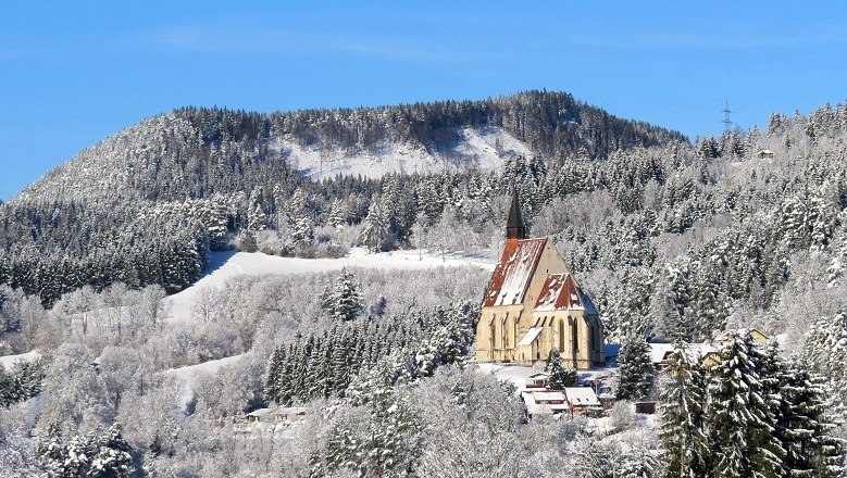 Wolfgangskirche, © Marktgemeinde Kirchberg a.W./Wolfgang Riegler Winterlandschaft mit Kirche vor bewaldetem Hügel.