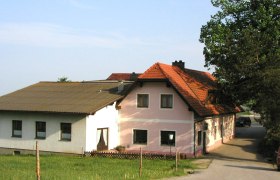 Gasthaus Brandstetter, © Gemeinde Hochneukirchen-Gschaidt Ein traditionelles Gasthaus mit rosa und weißen Wänden und einem roten Ziegeldach, umgeben von grüner Landschaft.