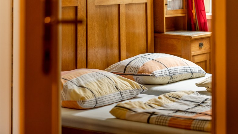 Bedroom, © Wiener Alpen / Christian Kremsl A cozy bedroom with wooden furniture and checkered pillows on the bed.