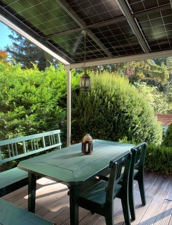 Terrace, © bed and pool Terrace with green table and benches, surrounded by bushes and trees, with solar panel roof.