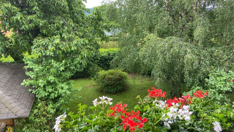 Ausblick vom Gästebalkon, © Wiener Alpen Blick vom Balkon auf einen grünen Garten mit Bäumen und roten sowie weißen Blumen im Vordergrund.