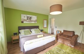 Zimmer Veltliner, Gästezimmer Victoria, © Marianne Graf Modern eingerichtetes Gästezimmer mit grünem Akzent, Doppelbett, braunem Sessel und dekorativem Bild an der Wand.