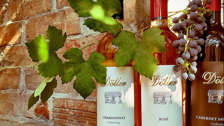 Viticulture Döller, © Familie Döller Three Döller wine bottles in front of a brick wall with vine leaves and grapes.
