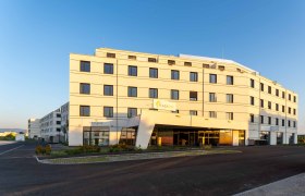 Plaza INN, © Plaza INN Ein modernes, mehrstöckiges Gebäude mit der Aufschrift 'Plaza INN' bei Sonnenuntergang.