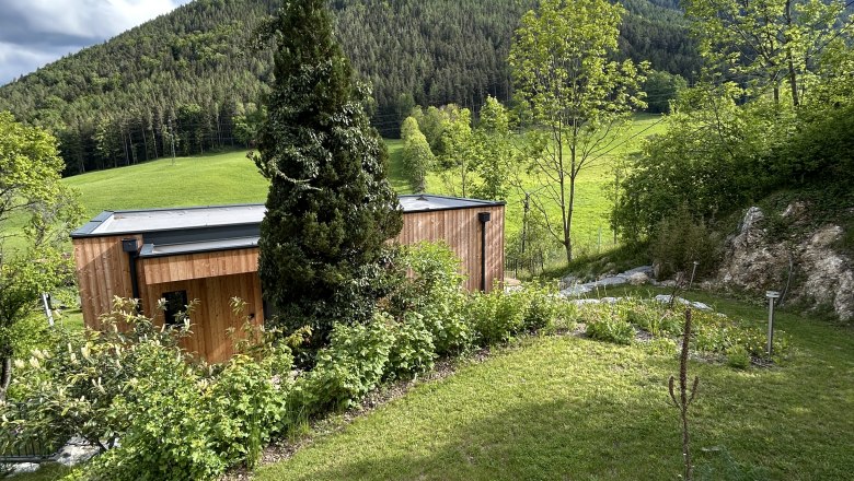 Feigenterrasse am Semmering, © Stupacher Holzhaus mit Garten vor bewaldetem Hügel und blauem Himmel.