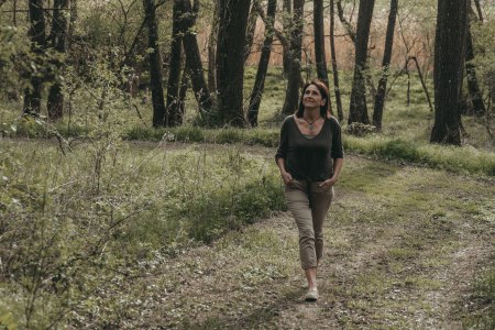 Raum für bewusst sein & nat-ur-vertrauen, © Ines Steiner Frau spaziert auf einem Waldweg, umgeben von Bäumen und Grün.