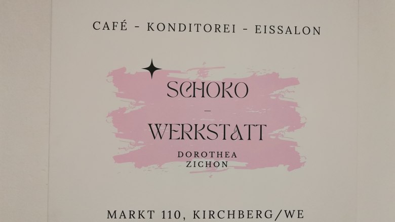 Charmantes Kaffeehaus mit Gastgarten, © Wiener Alpen Schild der Schoko-Werkstatt in Kirchberg mit rosa Hintergrund.