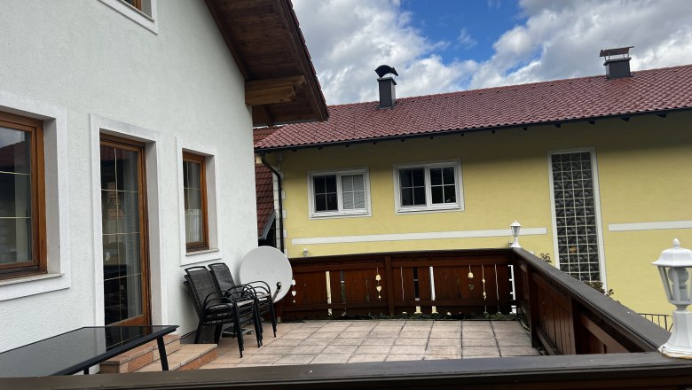 Terrasse vom Apartement, © Andrea Tauchner Terrasse eines Apartments mit Holzmöbeln und Blick auf ein gelbes Nachbarhaus mit rotem Dach.