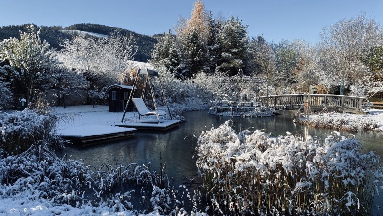 Paradiesgartl im Winter, © Peter Pichler Verschneiter Garten mit Teich, Brücke und Schaukel im Winter.