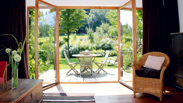 Ferienhaus Unternberg - Terrasse, © Fam. Gruber-List Blick von einem Wohnzimmer auf eine Terrasse mit Gartenmöbeln und grünem Garten.