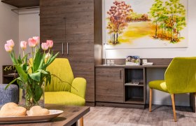 Paket Carpe diem Appartement, © Vitalzeit Hotel Weber Gemütliches Zimmer mit grünen Sesseln, Tulpen auf dem Tisch und einem Landschaftsbild an der Wand.