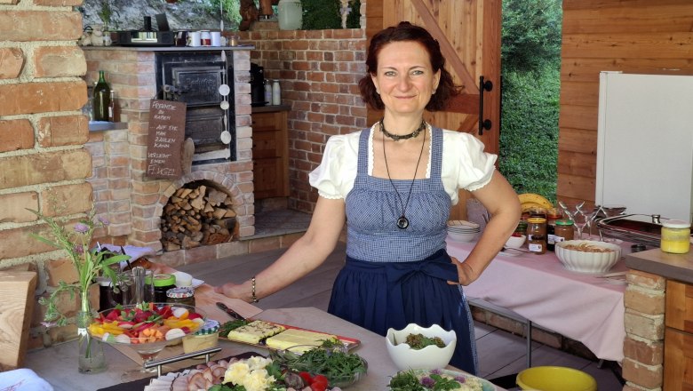 Sonntagsbrunch in Mei Kuchl, © Anita Brem-Hofer Die Chefin in traditioneller Kleidung in einer rustikalen Küche mit Speisen.
