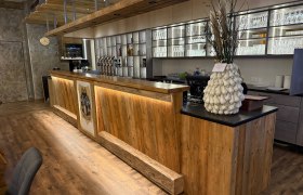 Restaurant Osterbauer, © Thomas Osterbauer Holztheke in einem Restaurant mit dekorativer Vase und Gläserregal im Hintergrund.