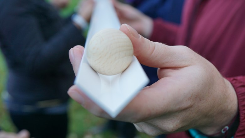 Teamwandern Incentives, © Wolfgang Menzel Nahaufnahme einer Hand, die eine weiße Rinne mit einer Holzkugel darin hält.