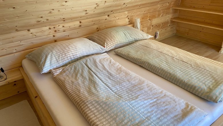 Doppelzimmer, © Wiener Alpen Doppelbett in einem Zimmer mit Holzverkleidung.