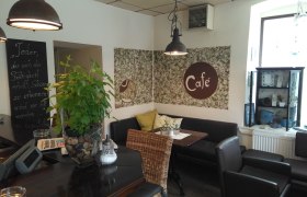 Innenraum, © Fam.Hausmann Gemütliches Café mit Pflanzen, Sitzgelegenheiten und Dekorationen.