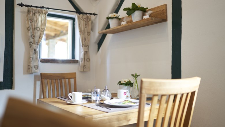 Breakfast room, Victoria guest room, © Marianne Graf A cozy breakfast room with a wooden table, chairs and decorative plants on a shelf.