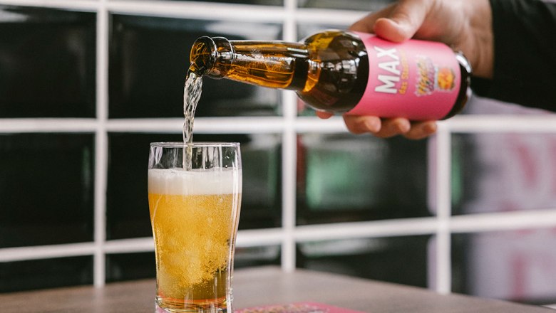 Siegl's am Markt - selbst gebrautes Stadtbier MAX, © Wiener Alpen/Sophie Menegaldo Eine Hand gießt Bier aus einer Flasche mit dem Etikett 'MAX' in ein Glas auf einem Tisch.