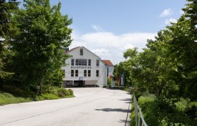 Hausansicht Waldpension, © ÖJAB Waldpension Ansicht der Waldpension mit Bäumen und Fahnen im Vordergrund.