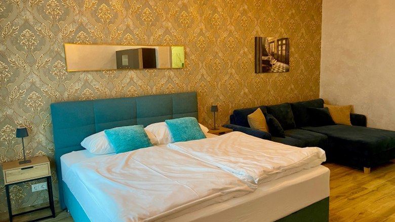 Zemlinsky Hof, © Wiener Alpen Elegantes Hotelzimmer mit Doppelbett, blauer Couch und goldener Tapete.