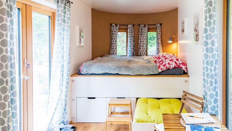 Schlafbereich Ronja, © WW Wohnwagon GmbH Gemütlicher Schlafbereich mit Hochbett, Vorhängen und kleinem Tisch in einem hellen Raum.