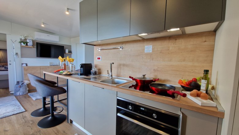 Küche des Johannesbachklamm Chalet, © Johannesbachklamm Chalet Moderne Küche mit grauen Schränken, Herd, Spüle und Barhockern.