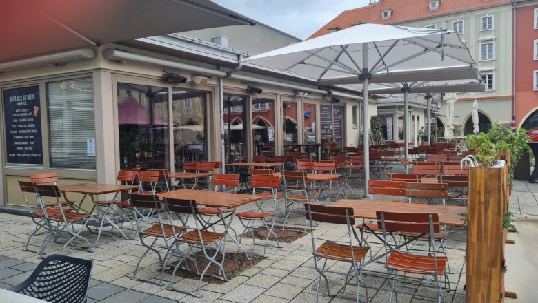 Siegl's Pub, © Siegl's Pub Außenbereich eines Pubs mit leeren Holztischen und Stühlen unter großen Sonnenschirmen.