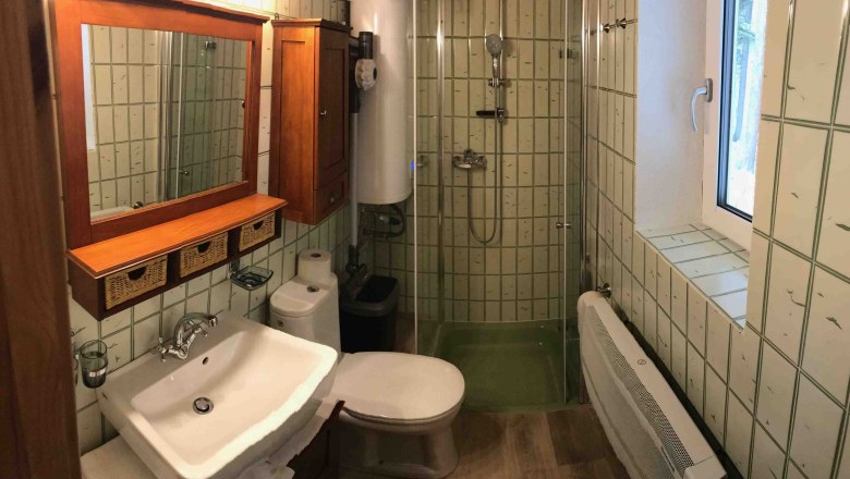 Ferienhaus, © Marianne Gschaider Kleines Badezimmer mit Dusche, Waschbecken, Toilette und Holzschränken.