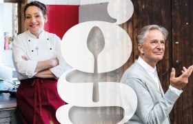 Kräuterwirtin Gerda Stocker mit Autor, Erzähler und Märchendichter Folke Tegetthoff, © Nicole Heiling, Nikolaus Pfusterschmid Eine Frau in Kochkleidung und ein Mann in grauem Pullover stehen nebeneinander, getrennt durch ein großes, stilisiertes G-Symbol.