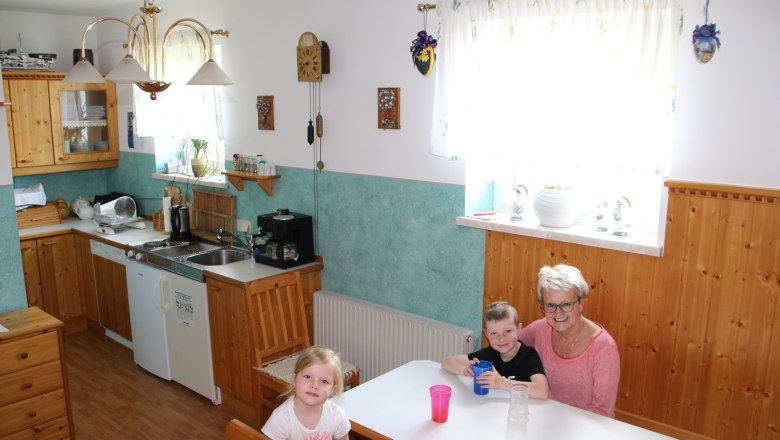 Breakfast room, © Karl Buchner A breakfast room with wooden furniture, a kitchen in the background and three people at a table.