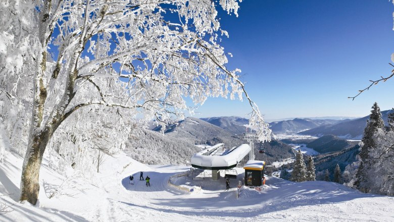 Bergstation Sessellift - © schneebergbahn.at, © schnneebergbahn.at Winterlandschaft mit Sesselliftstation, verschneiten Bäumen und Bergen im Hintergrund.