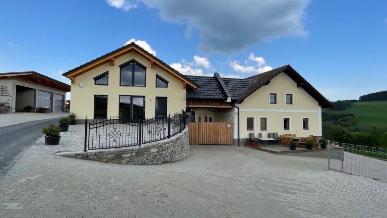 Biohof Bernsteiner, © Gerhard Heinrich Gelbes Haus mit großen Fenstern auf gepflasterter Fläche unter blauen Himmel.