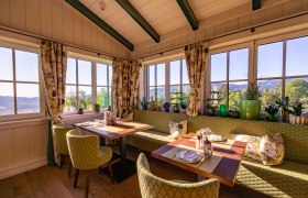 Hotel & Restaurant Knappenhof, © Niederösterreich Werbung / Maximilian Pawlikowsky Gemütlicher Essbereich mit großen Fenstern, grünen Polstermöbeln und Pflanzen, mit Blick auf die Landschaft.