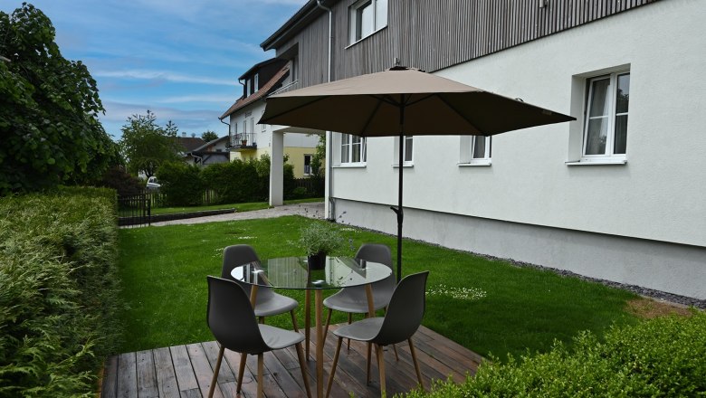 Gemütlicher Sitzbereich im Garten, © Christine Kuppelwieser Garten mit Sitzbereich, Tisch, Stühlen und Sonnenschirm auf Holzterrasse.