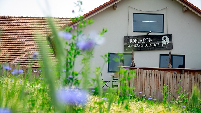 Farm store, © Sooo gut schmeckt die Bucklige Welt/ Viktoria Kornfeld Exterior view of Mandl's Ziegenhof farm store with wooden fence and flowers in the foreground.
