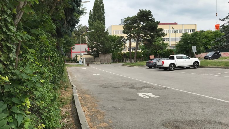 Camping Abstellplatz, © Birgit Rada-Tomasin Parkplatz mit Autos und Bäumen, Gebäude im Hintergrund.